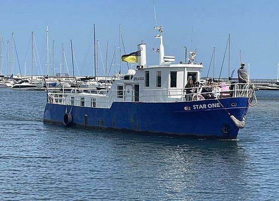 Do portu wpływa nIebiesko-biały kuter, na dziobie grupa