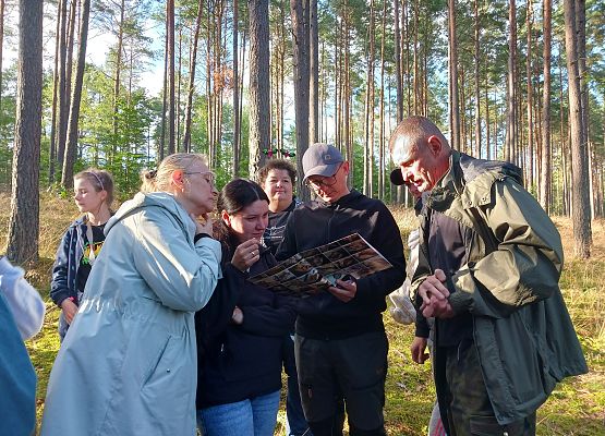 Grupa ludzi stojąca w lesie ogląda plakat z sylwetkami nietoperzy.