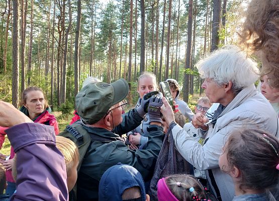 Grupa ludzi w lesie patrząca na nietoperza, ktorego trzyma prowadzący zajecia Józef Wysiński  w rękach ubranych w rękawiczki