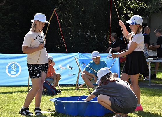 Troje dzieci łowi wędkami drewniane rybki z opisami