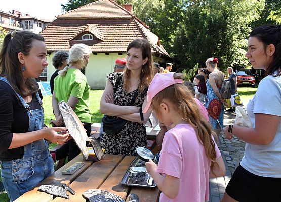 Pani prezentuje model płomykówki. Dwie panie i dziewczynka słuchają. Dziewczynka ogląda przez lupę sowie wypluwki