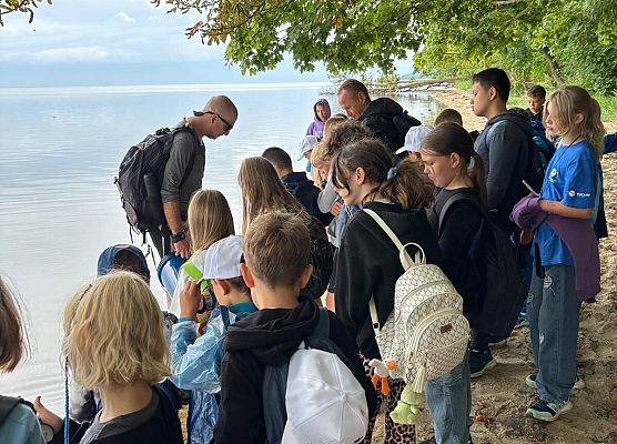 grupa ok 30 osób stoi na wąskiej plaży nad Zatoka.