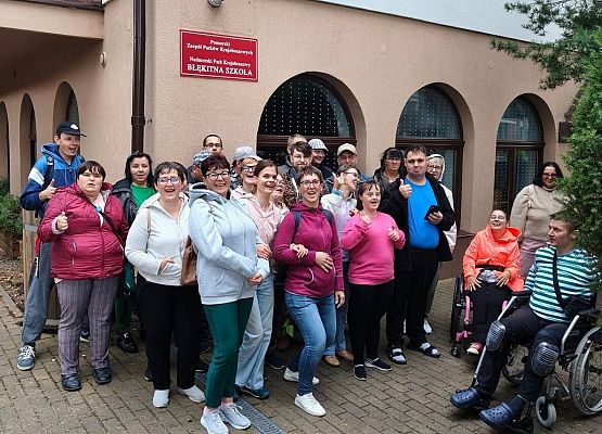 Cała grupa ok 30 os. przed budynkiem Błękitnej Szkoły. Po prawej 2 osoby na wózku inwalidzkim