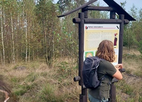 Spacer z okazji Dnia Parków Krajobrazowych „W poszukiwaniu archeofitów” fot. Karolina Rozmarynowska Przewodniczka przy tablicy opisującej obrządek pogrzebowy kultury wielbarskiej.