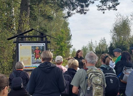 Spacer z okazji Dnia Parków Krajobrazowych „W poszukiwaniu archeofitów” fot. Karolina Rozmarynowska Przystanek w trakcie spaceru. uczestnicy słuchają przewodniczki stojącej przy tablicy z rysunkiem Gota.