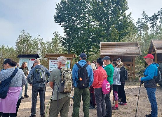 Spacer z okazji Dnia Parków Krajobrazowych „W poszukiwaniu archeofitów” fot. Karolina Rozmarynowska Uczestnicy spaceru na miejscu startu. Kolorowo ubrani ludzie, w tle tablica z mapą Zaborskiego Parku Krajobrazowego.