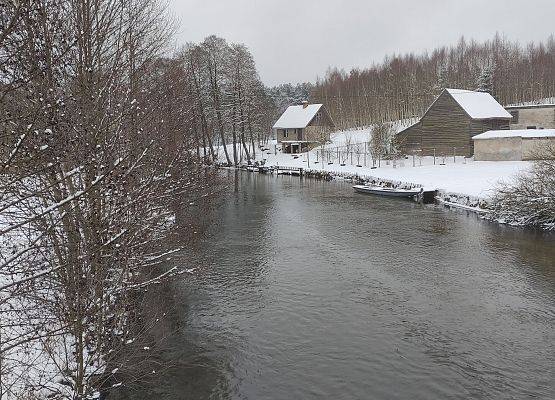 Zimowy krajobraz, rzeka. Na jej brzegu domy.