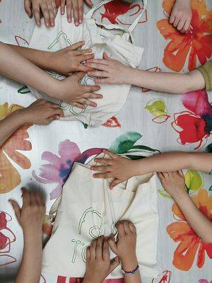 Ulewa przegoniła nas z lasu, więc część zabaw zrobiliśmy w sali, fot. JKR Dłonie kilku dzieci dotykają czegoś schowanego w dwóch bawełnianych torbach.