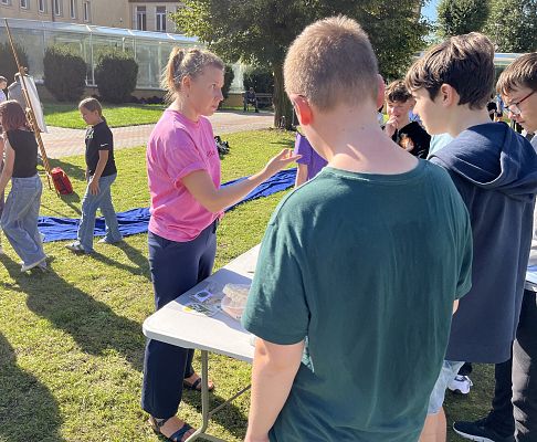 Jak to nie wiesz który to trzmiel? fot. AB grupa młodzieży przy stole, w centralnym punkcie kobieta, która pokazuje coś palcem z surową miną.